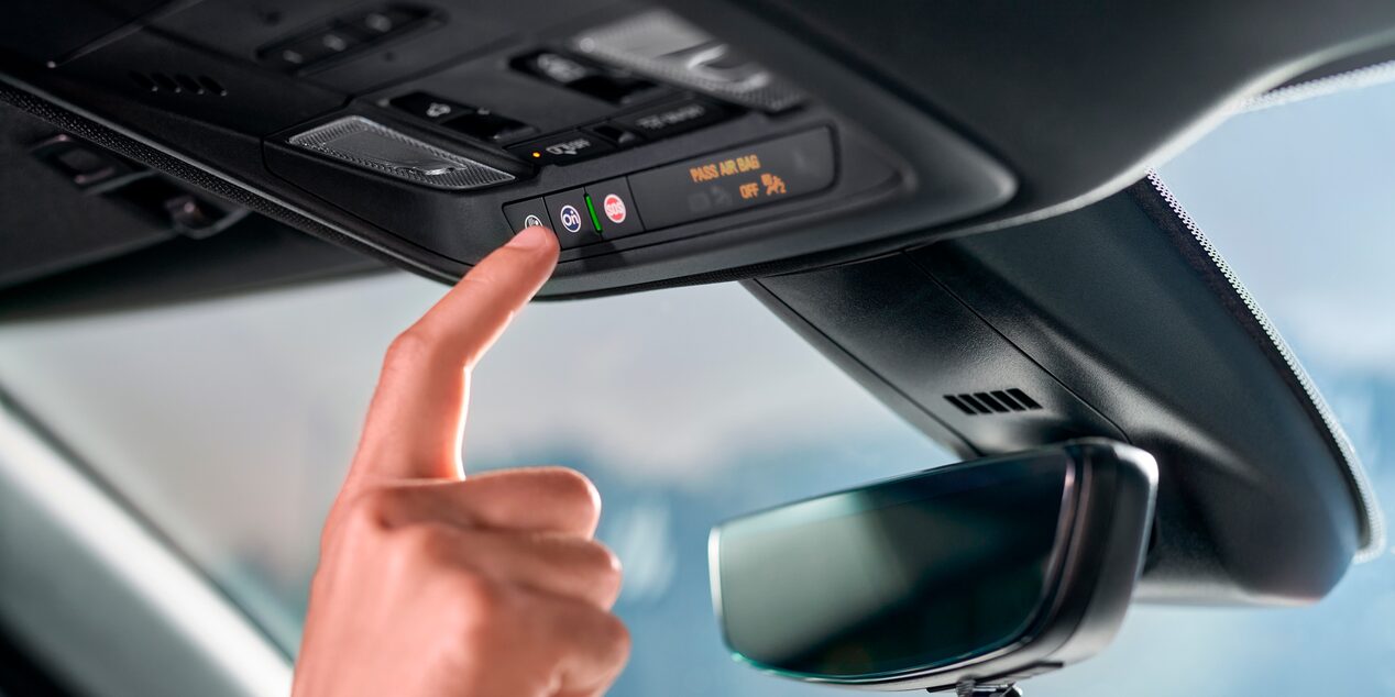 Imagen de una mano activando el botón OnStar en la parte superior de un vehículo Chevrolet.