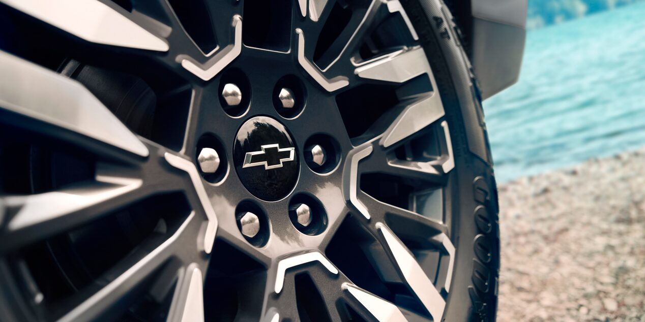 Imagen en primer plano del rin de un vehículo Chevrolet con un lago de fondo.